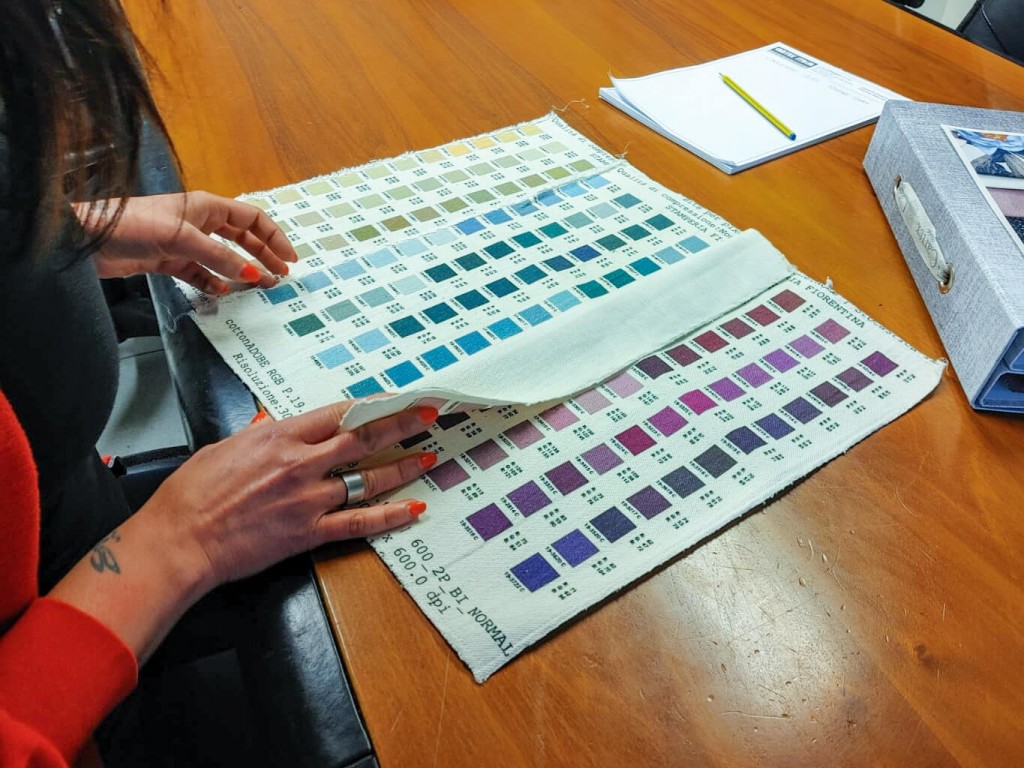 Hands with red nail polish on their fingers flicking through the colour chart of a fabric printer